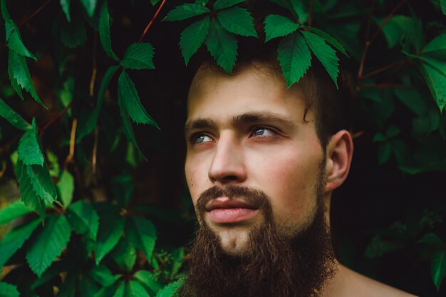 portret przystojny mężczyzna na zielone letnie liście. Moda Brunetka mężczyzna z niebieskimi oczami, portret w dzikich liściach (winogrona), naturalne tło.