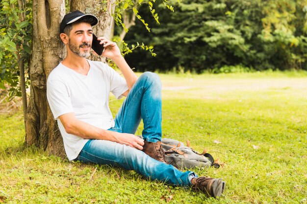 Portret przystojny mężczyzna siedzi pod drzewem rozmawia przez telefon komórkowy w parku