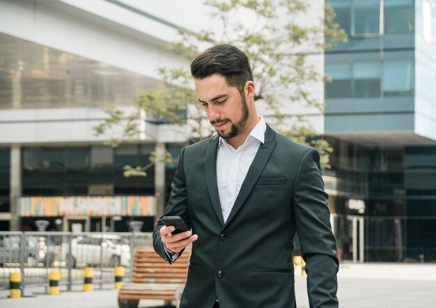 Portret przystojny młody biznesmen robi wiadomości tekstowej na telefonie komórkowym