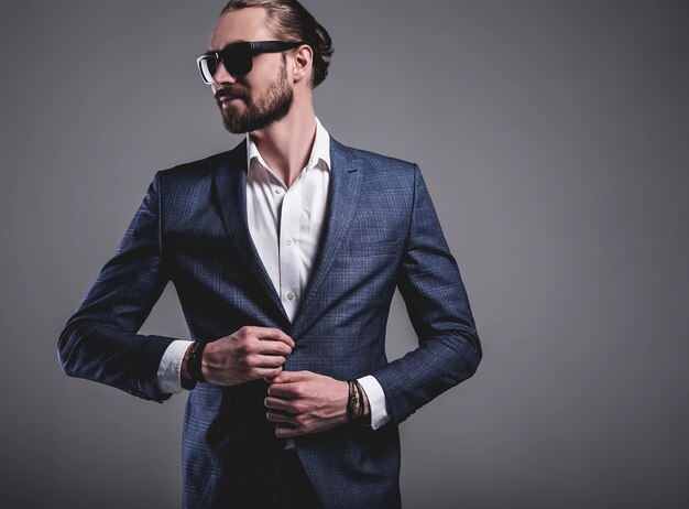 portret przystojny moda model hipster stylowy biznesmen biznesmen ubrany w elegancki niebieski garnitur w okulary przeciwsłoneczne pozowanie na szaro