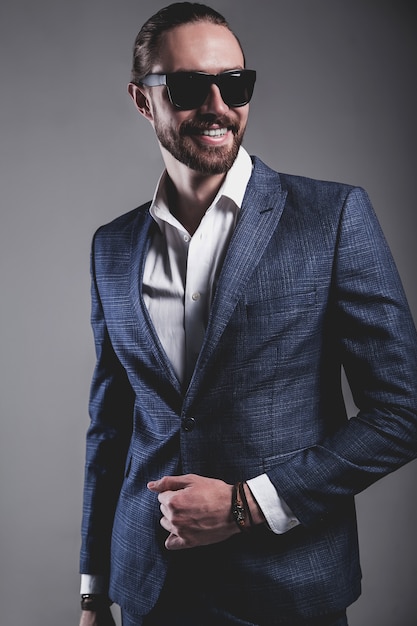 portret przystojny moda model hipster stylowy biznesmen biznesmen ubrany w elegancki niebieski garnitur w okulary przeciwsłoneczne pozowanie na szaro