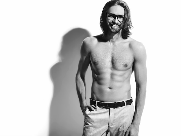 portret przystojny moda stylowy hipster model mężczyzna z gołą klatką piersiową w okularach na białym tle. Z jedną ręką w kieszeni