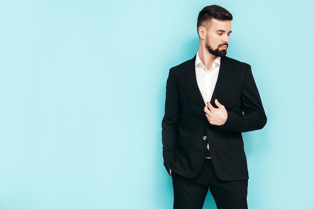 Portret przystojny pewnie stylowy hipster lamberseksualny model seksowny nowoczesny mężczyzna ubrany w elegancki czarny garnitur Moda mężczyzna pozuje w studio w pobliżu niebieskiej ściany