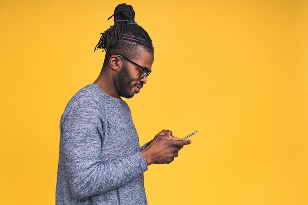 Portret przystojny podekscytowany wesoły radosny afroamerykanin czarny facet ubrany dorywczo wysyłanie i otrzymywanie wiadomości do swojego kochanka na białym tle nad żółtym tle. za pomocą telefonu.