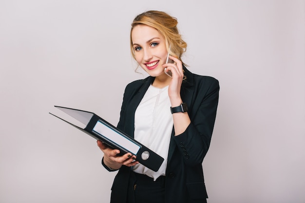 Bezpłatne zdjęcie portret radosna blondynka businesswoman rozmawia przez telefon, trzymając folder, uśmiechając się odizolowane. ubrana w białą koszulę i czarną marynarkę, nowoczesny pracownik biurowy, elegancki, kariera