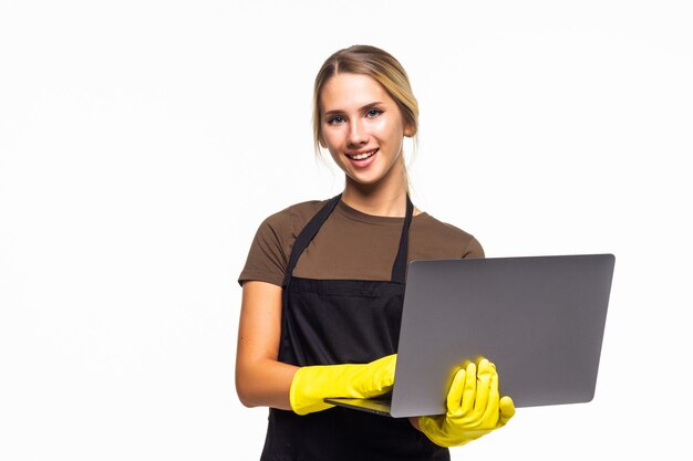 Portret radosnej gospodyni domowej w żółtych gumowych rękawiczkach trzymająca laptopa podczas czyszczenia na białym tle nad białym