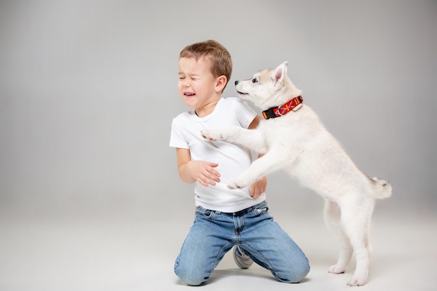 Portret radosny mały chłopiec zabawy z siberian husky szczeniaka na podłodze w studio. Zwierzę, przyjaźń, miłość, zwierzę domowe, dzieciństwo, szczęście, pies, koncepcja stylu życia