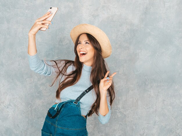 Portret rozochocona młoda kobieta bierze fotografii selfie i jest ubranym nowożytnych ubrania i kapelusz. . Pokazuje znak pokoju