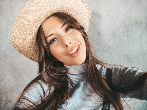 Portret rozochocona młoda kobieta bierze fotografii selfie z inspiracją i jest ubranym nowożytnych ubrania i kapelusz.