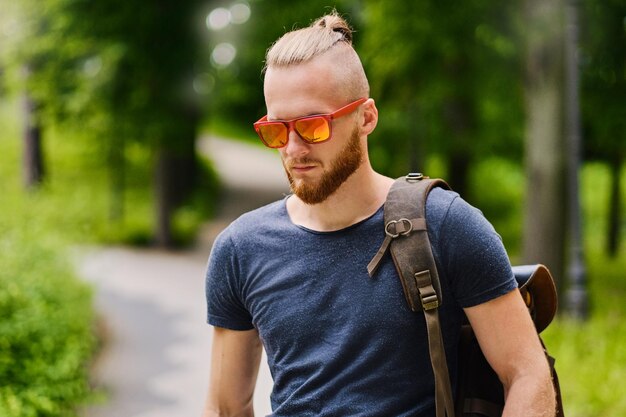 Portret rudy mężczyzna w okularach przeciwsłonecznych nad dzikim parkiem miejskim.