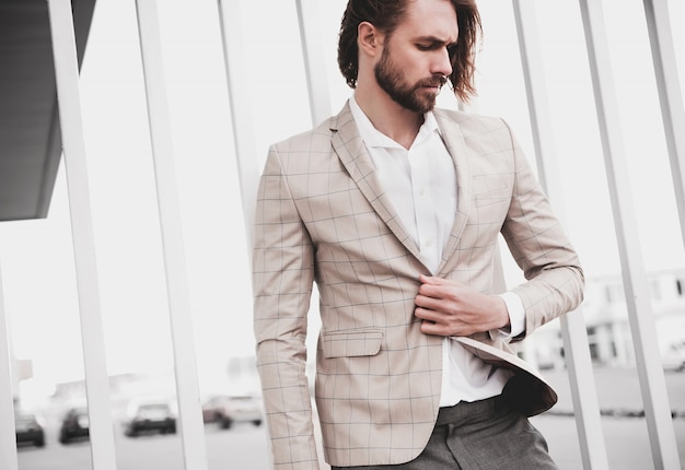 portret seksowny przystojny moda mężczyzna model mężczyzna ubrany w elegancki beżowy kratkę garnitur pozowanie na tle ulicy