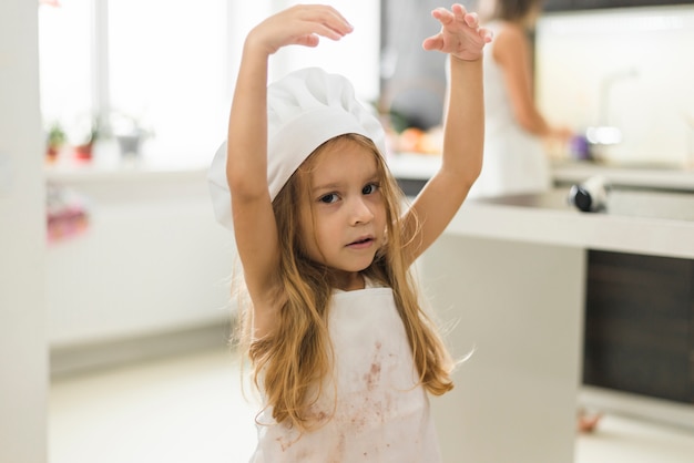 Portret śliczna dziewczyna jest ubranym szefa kuchni kapelusz z jej ręką podnoszącą