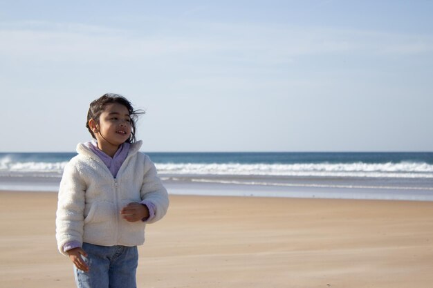 Portret śliczna mała Azjatycka dziewczyna. Modelka z ciemnymi włosami i biały sweter uśmiecha się do kamery. Portret, koncepcja piękna