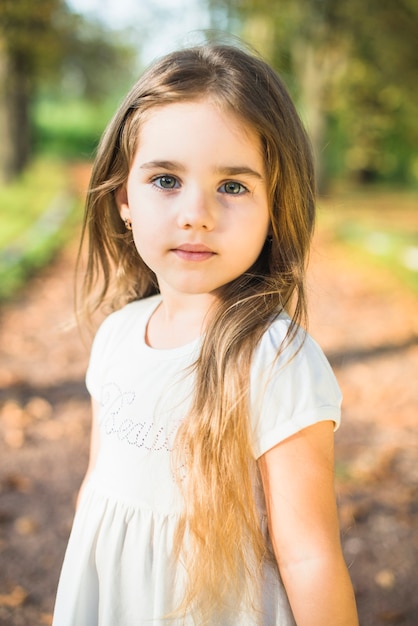 Portret śliczna mała dziewczynka z długie włosy pozycją w parku
