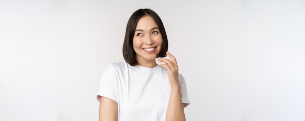 Portret ślicznej zalotnej kobiety śmiejącej się i uśmiechającej się patrząc na bok przemyślane myślenie lub obrazowanie czegoś stojącego w białej koszulce na tle studia