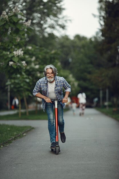 Portret starszego mężczyzny z hulajnogą w letnim parku