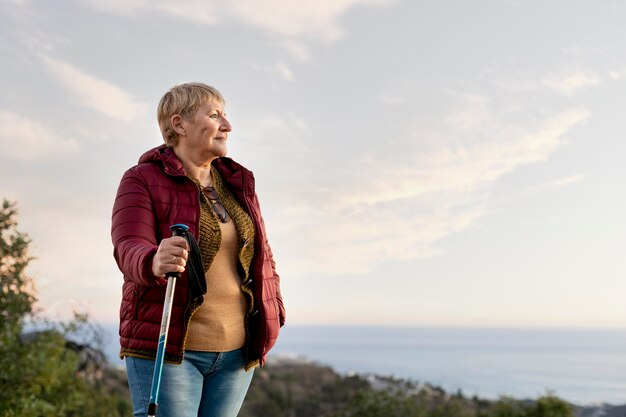 Portret starszej kobiety podczas przygody z naturą, trzymającej kij trekkingowy