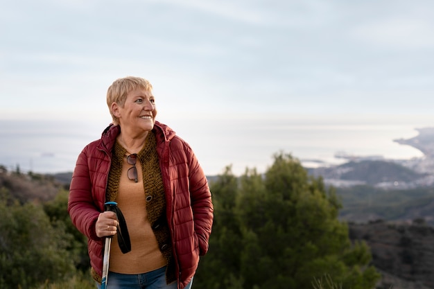 Portret starszej kobiety podczas przygody z naturą, trzymającej kij trekkingowy