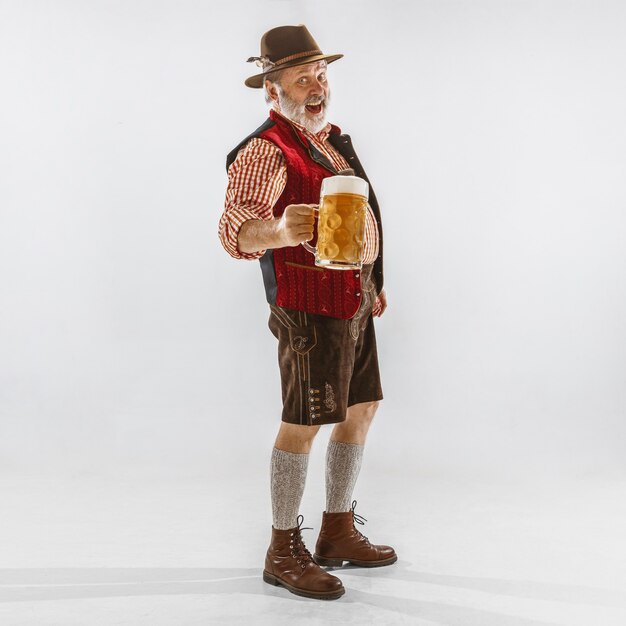 Portret starszy mężczyzna Oktoberfest w kapeluszu, ubrany w tradycyjne bawarskie stroje. Mężczyzna pełnej długości strzał w studio na białym tle. Uroczystość, święta, koncepcja festiwalu. Pić piwo.