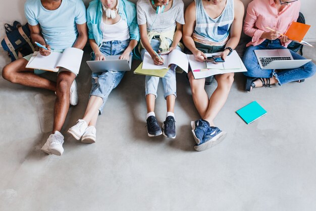 Portret studentów w modnych trampkach, schładzających się na podłodze, przygotowujących się do wspólnych egzaminów. Przyjaciele z uniwersytetu spędzają razem czas przy laptopach i pisząc streszczenie.