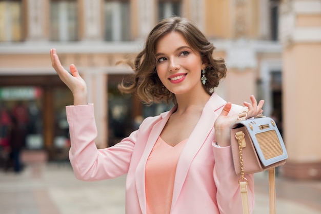 Bezpłatne zdjęcie portret stylowej pięknej kobiety spacerującej w centrum miasta w różowej kurtce trzymającej torebkę, letni trend mody, uśmiechnięty, szczęśliwy, naturalny makijaż, falujące włosy, elegancka dama, romantyczny nastrój