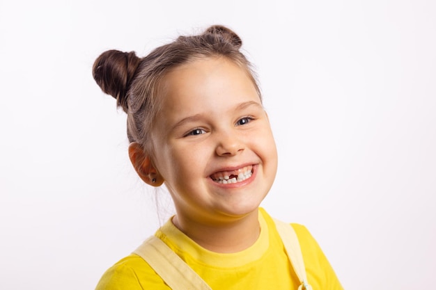 Portret świecącego małego dziecka pokazujący brakujący przedni ząb dziecka i uśmiechający się odwracający wzrok w żółtym t...