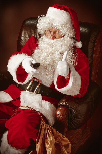Portret Świętego Mikołaja w czerwonym kostiumie z pilotem do telewizora