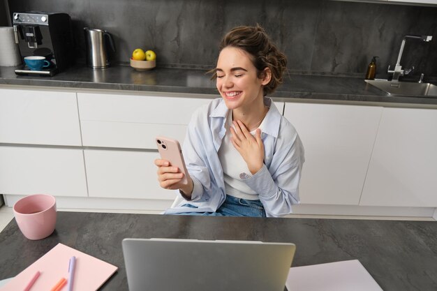 Portret szczerej młodej kobiety śmiejącej się za pomocą laptopa i smartfona wideo czatu dołączając do rozmów online