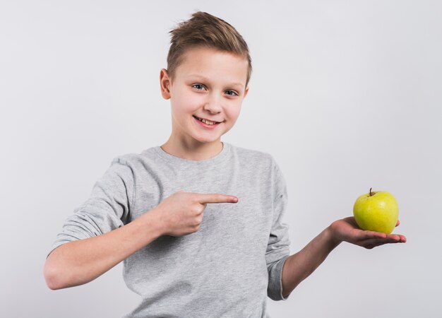 Portret szczęśliwa chłopiec wskazuje jego palec w kierunku całego zielonego jabłka w ręce