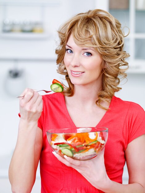 Portret szczęśliwa kobieta jedzenie sałatki z warzyw w kuchni