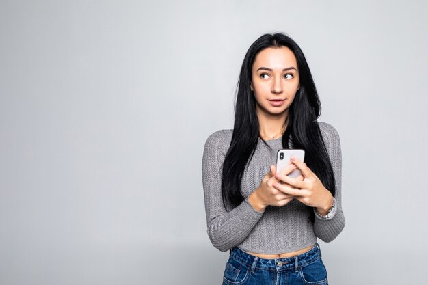 Portret szczęśliwa młoda dziewczyna używa smartphone odizolowywającego na szarej ścianie