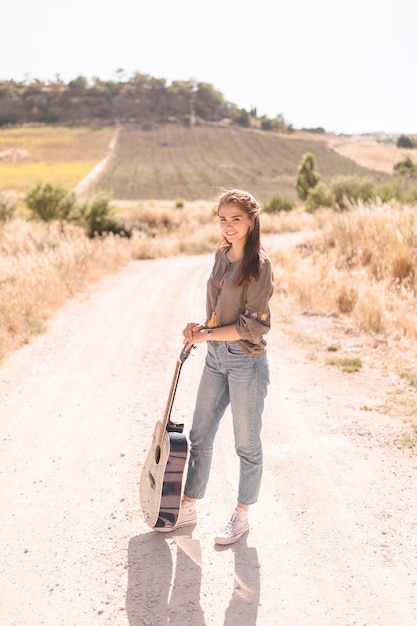 Portret szczęśliwa nastoletnia dziewczyna z gitary pozycją na drodze polnej