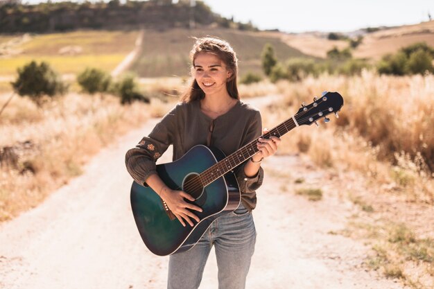 Portret szczęśliwa nastoletniej dziewczyny pozycja na drodze polnej bawić się gitarę
