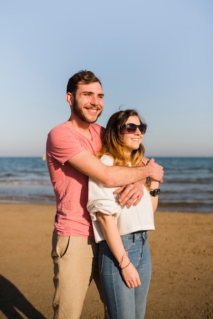 Bezpłatne zdjęcie portret szczęśliwa pary pozycja blisko seashore patrzeje daleko od przy plażą