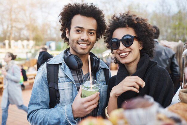 Portret szczęśliwa śliczna ciemnoskóra para z fryzurą afro, spacerująca po festiwalu żywności, degustacja i picie koktajlu