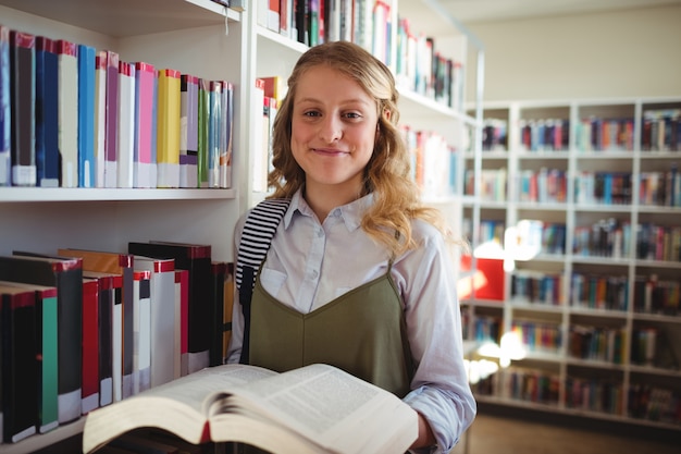 Portret szczęśliwa uczennica trzyma książkę w bibliotece