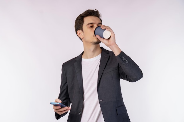 Portret szczęśliwego biznesmena używającego smartfona i pijącego kawę na białym tle