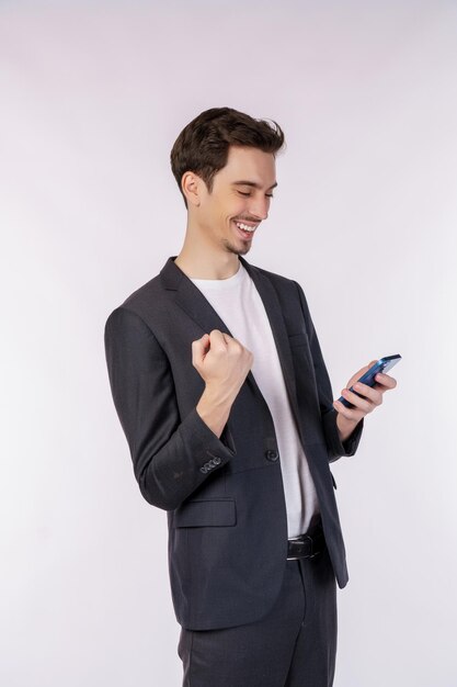 Portret szczęśliwego biznesmena używającego smartfona i wykonującego gest zwycięzcy zaciskającego pięść na białym tle