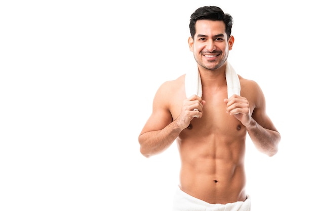 Portret szczęśliwego młodego mężczyzny z umięśnionym ciałem, stojącego w ręczniku, patrzącego na kamerę i uśmiechającego się