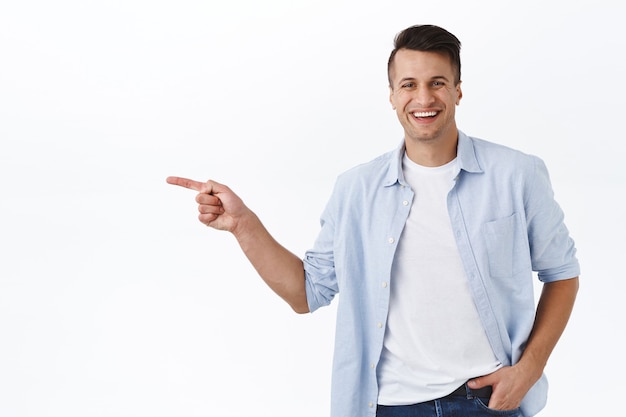 Portret szczęśliwego, przystojnego męskiego dorosłego mężczyzny wskazującego palcem w lewo i uśmiechniętego, polecam usługę lub produkt