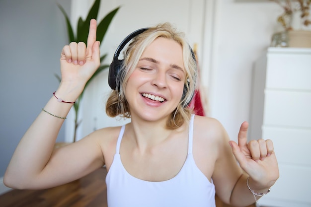 Bezpłatne zdjęcie portret szczęśliwej i beztroskiej blondynki słuchającej muzyki w bezprzewodowych słuchawkach tańczącej i