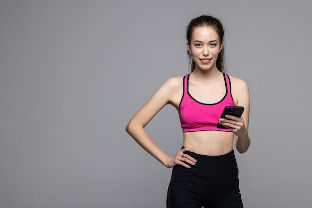 Portret szczęśliwej kobiety fitness stojącej i korzystającej z telefonu komórkowego na białym tle