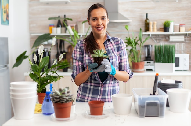 Portret szczęśliwej kobiety trzymającej soczystą roślinę siedzącą na stole w kuchni