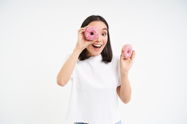 Portret Szczęśliwej Koreańskiej Kobiety Robi Okulary Z Dwóch Smacznych Przeszklonych Pączków Uśmiechając Się I Dobrze Się Bawiąc