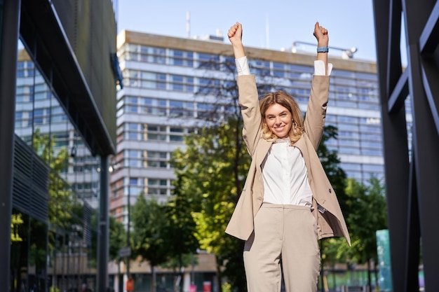 Portret szczęśliwej młodej bizneswomanu podnosi ręce do góry robi pompę pięściową świętuje zwycięstwo wygrywa coś achi