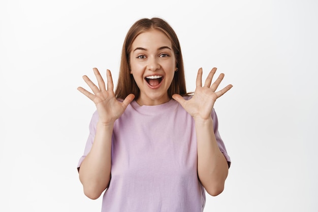 Bezpłatne zdjęcie portret szczęśliwej pięknej dziewczyny, radującej się, krzyczącej z radosnych i pozytywnych uczuć, ściskających dłonie i opowiadających wielkie wieści, niesamowite ogłoszenie, stojące na białym tle