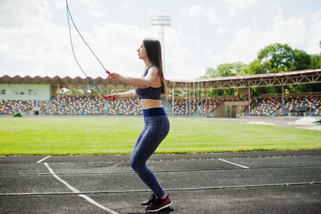 Portret szczęśliwej sprawnej młodej kobiety w odzieży sportowej, wykonującej ćwiczenia ze skakanką