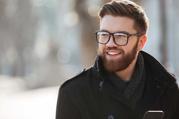 Portret szczęśliwy brodaty młody człowiek stoi outdoors w szkłach