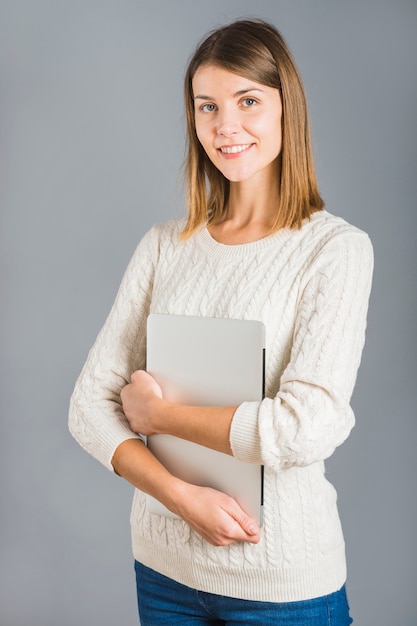 Portret szczęśliwy młodej kobiety mienia laptop na szarym tle