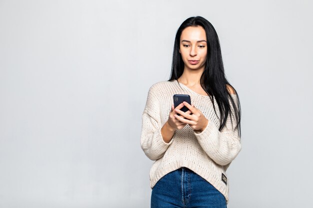 Portret szczęśliwy młodej kobiety mienia telefon komórkowy podczas gdy stojący i patrzejący daleko od nad szarości ścianą